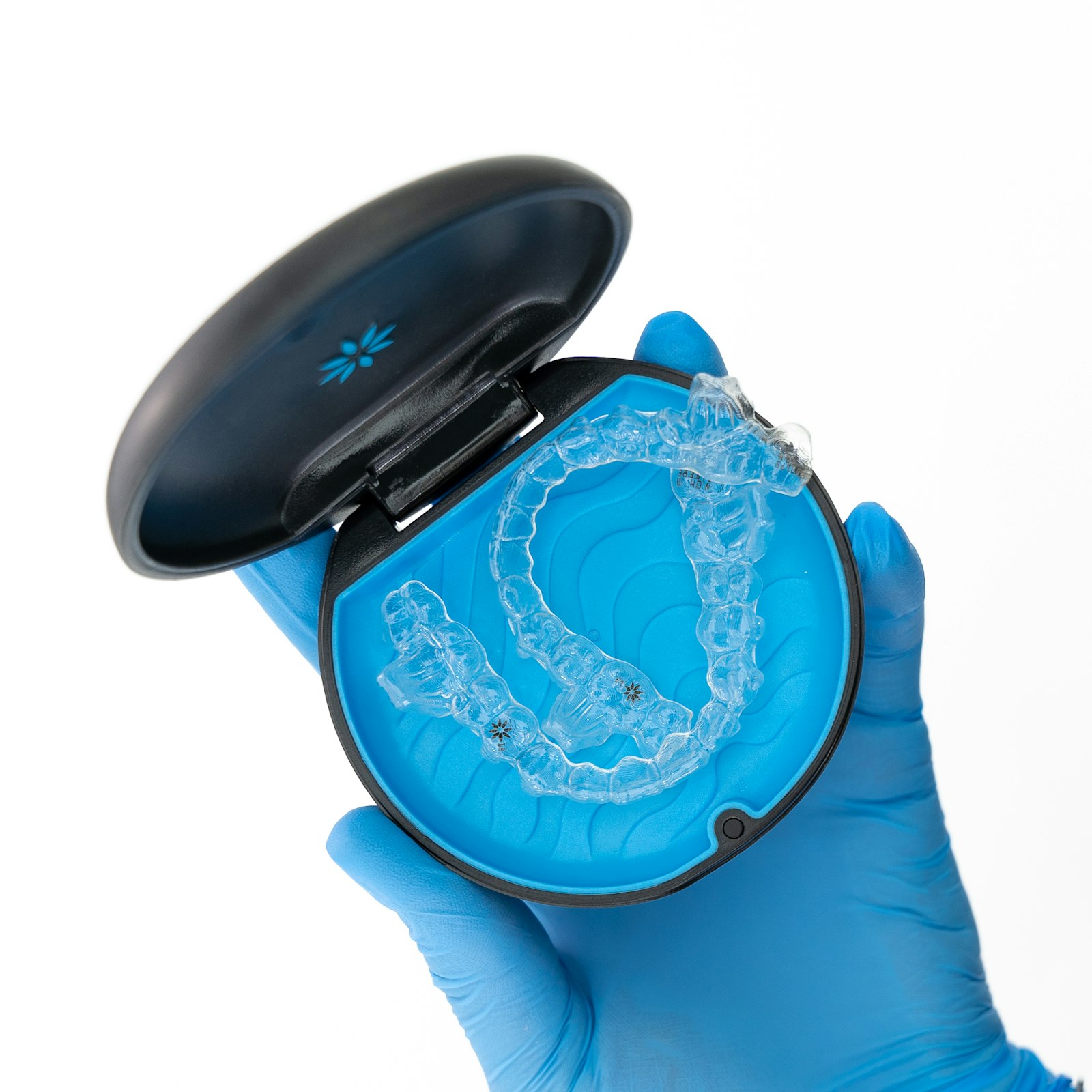 Gloved hand holding an open case with a clear dental aligner