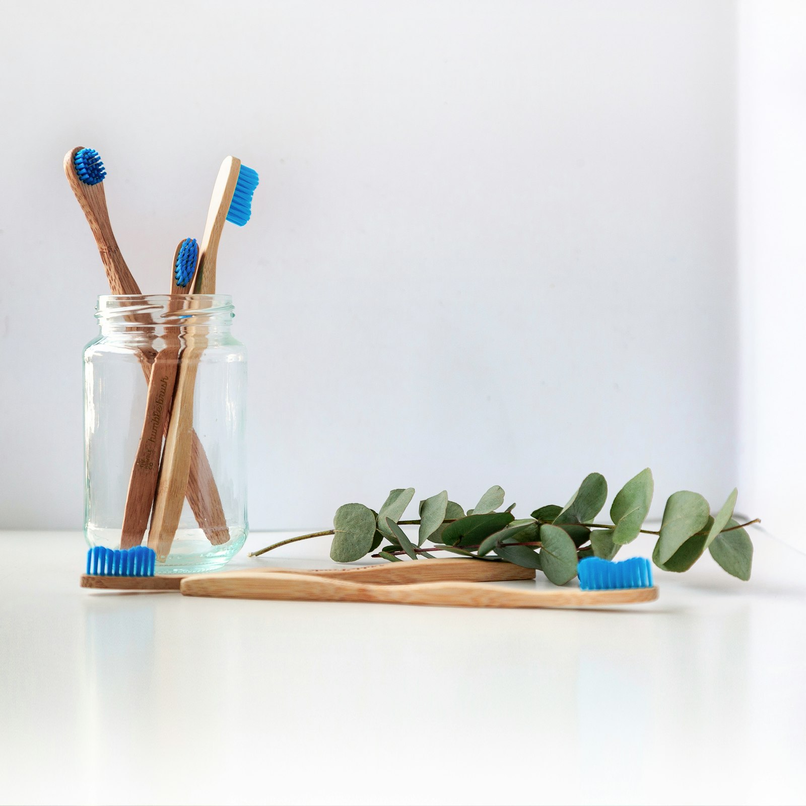 Toothbrushes in a clear glass jar on a white counter